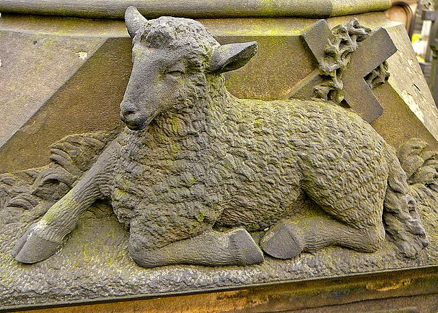 Stone carving of lamb with a cross in the background representing Jesus.