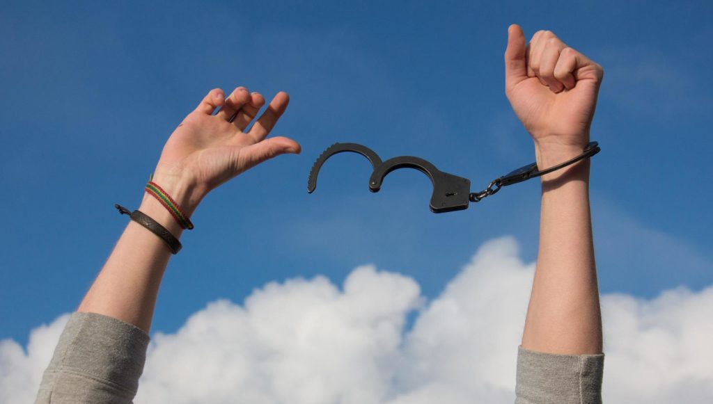 image of hands against the sky background with broken handcuffs representing the broken power of sin