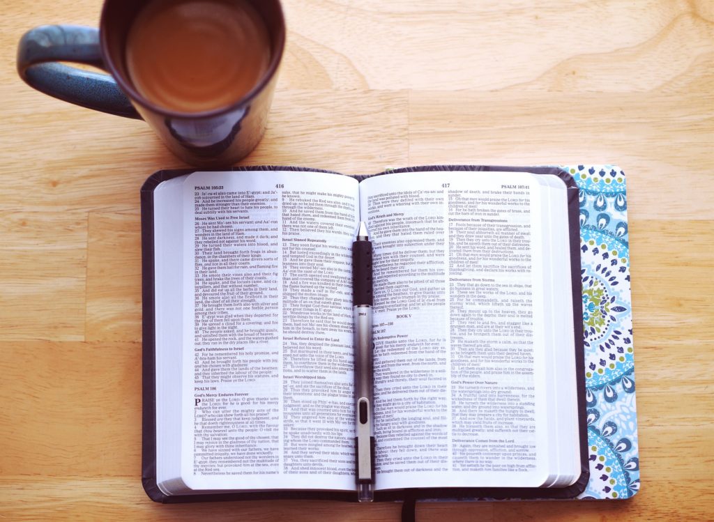 open bible representing reading the scripture; also a pen for taking notes, and a cup of coffee.